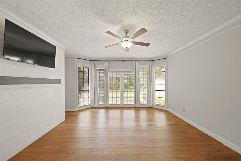 Primary bedroom has wood flooring and a wall of windows overlooking the backyard.