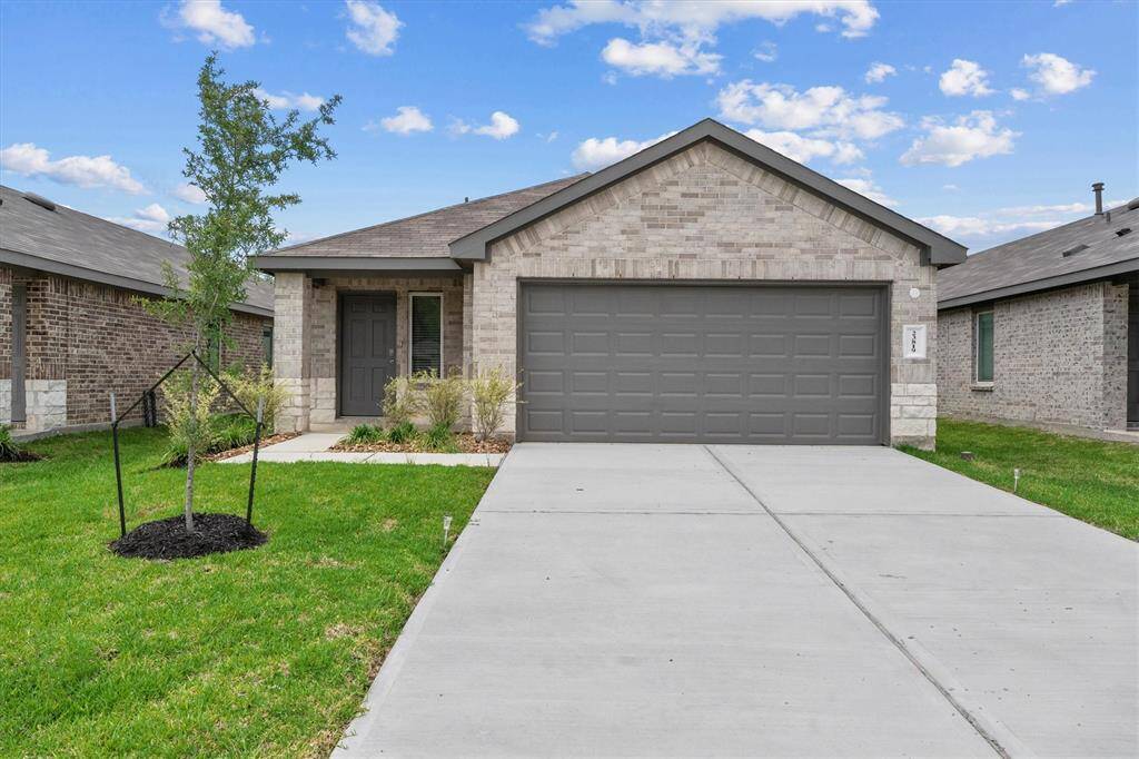 Charming curb appeal with a clean-lined façade featuring light brick with contrasting stone accents. A wide driveway leads to a 2-car garage with raised panel detailing and a cozy covered entryway with modern trim and a sleek front door.