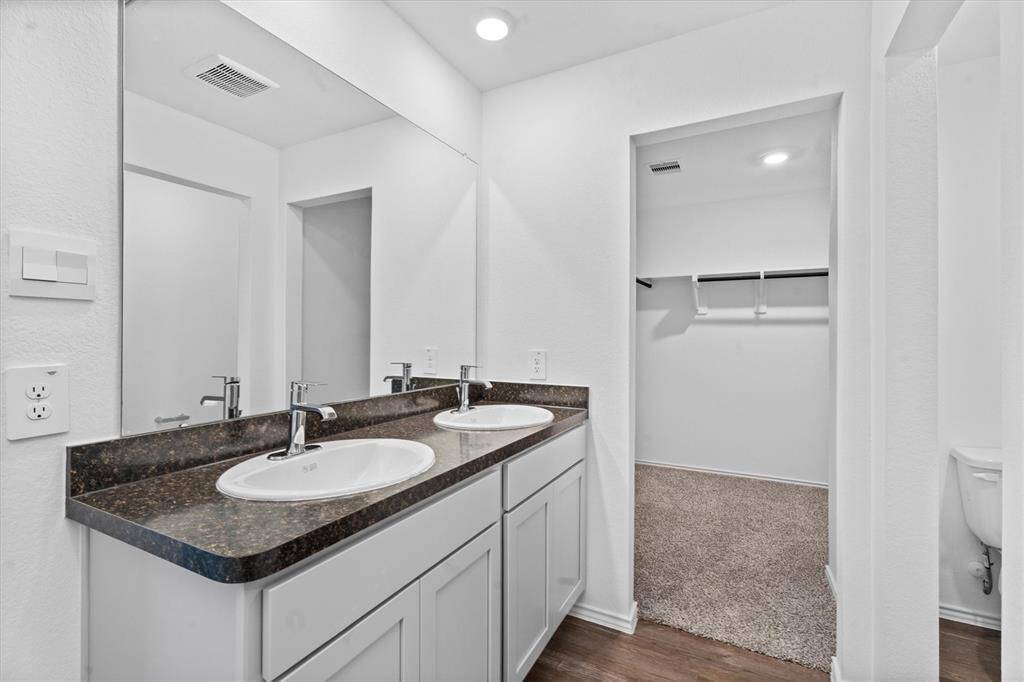 Features dual vanities with rich-toned counters, brushed nickel fixtures, and access to a large walk-in closet with built-in shelving and plenty of hanging space