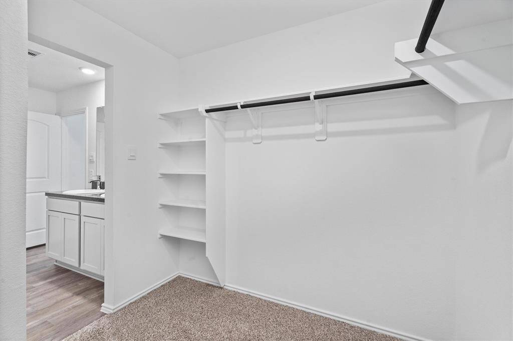 Features dual vanities with rich-toned counters, brushed nickel fixtures, and access to a large walk-in closet with built-in shelving and plenty of hanging space