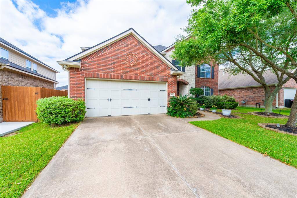 This photo showcases a charming two-story brick home with a double garage and a well-maintained lawn. A tree and shrubs add to the curb appeal, providing a welcoming entrance.