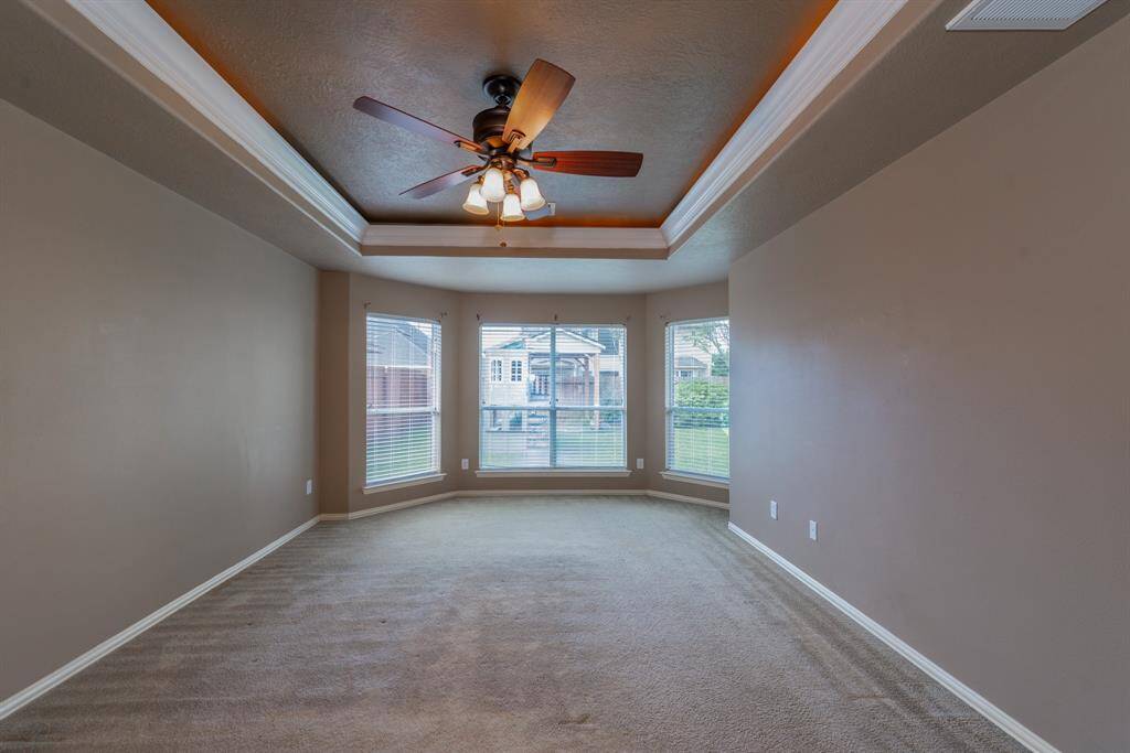 Discover the primary bedroom featuring a stunning wall of windows overlooking the backyard, complete with an elegant tray ceiling and a ceiling fan.