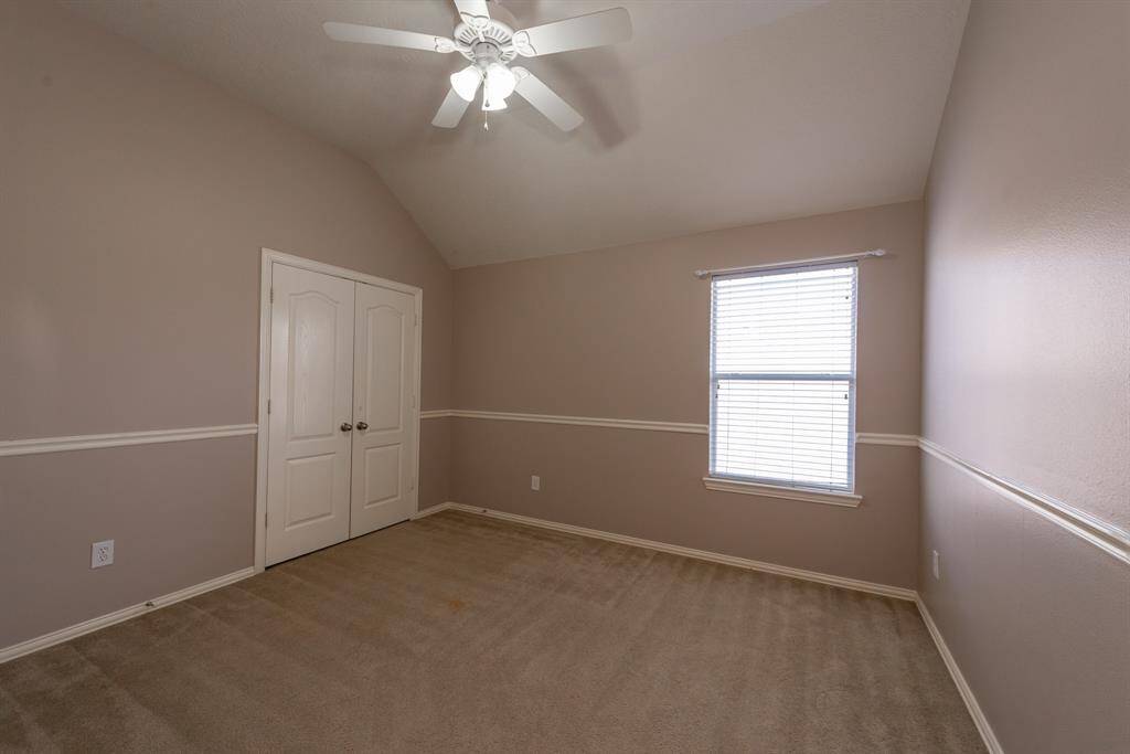 This room features neutral walls with a chair rail, a vaulted ceiling with a ceiling fan, carpeted flooring, a window with blinds for natural light, and double doors for easy access.