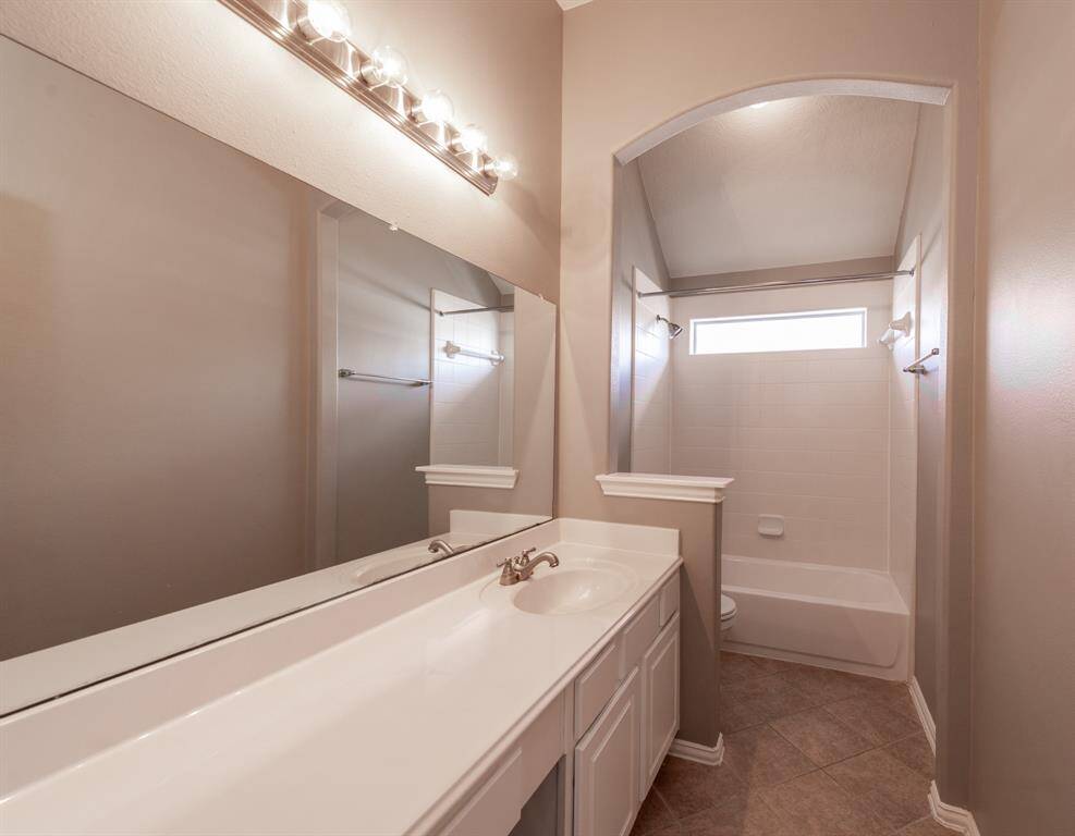 This bathroom features a modern design with a large mirror, ample lighting, and a spacious vanity. It includes a tub and shower combination with a window for natural light, all set against neutral tones for a clean, inviting feel.