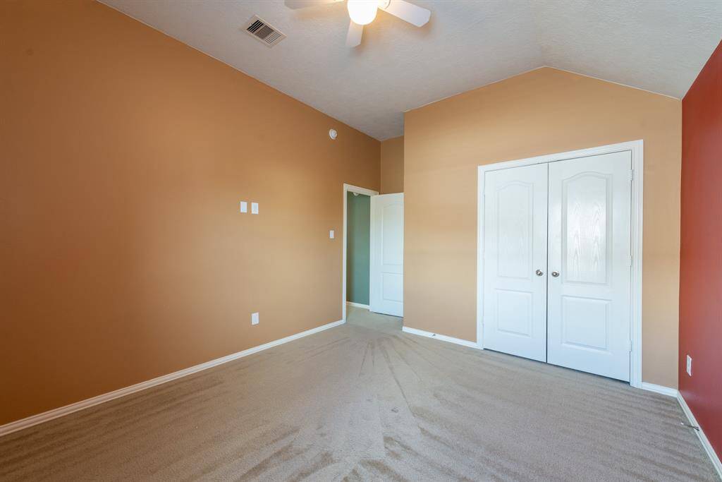 This photo shows a spacious, carpeted room with warm-toned walls, vaulted ceiling, ceiling fan, and a double-door closet. Ideal for a bedroom or home office.