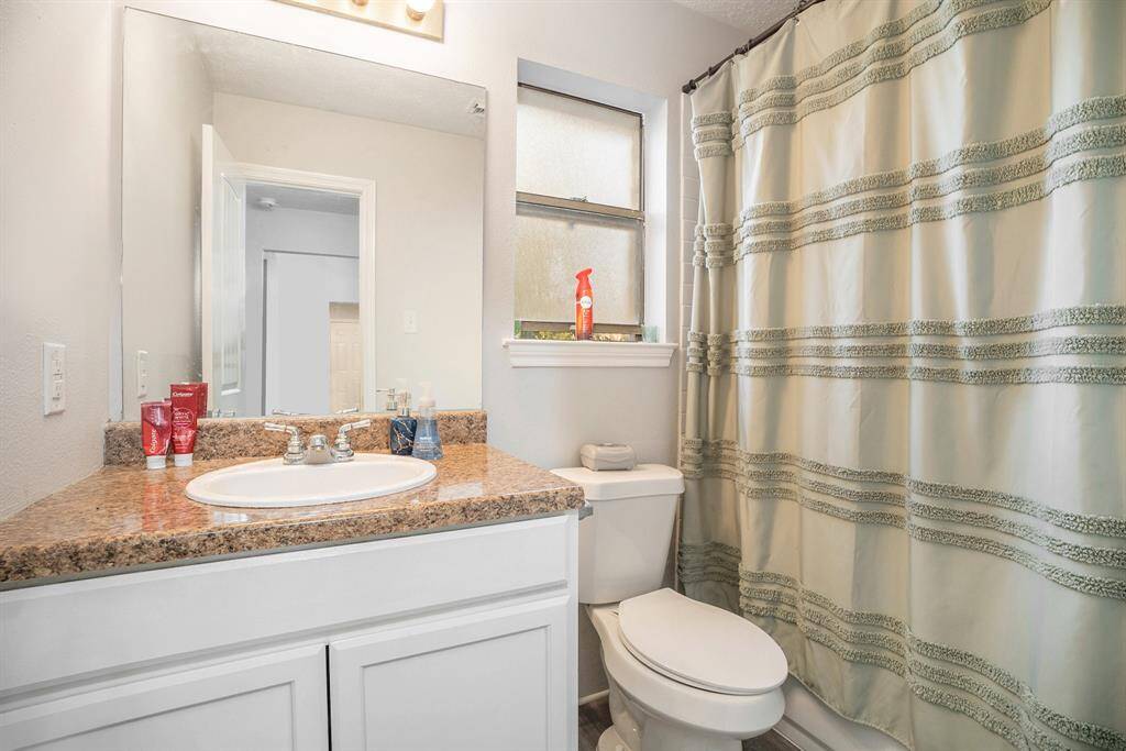 Full Bathroom with granite countertops, mirror and delicate white cabinetry.