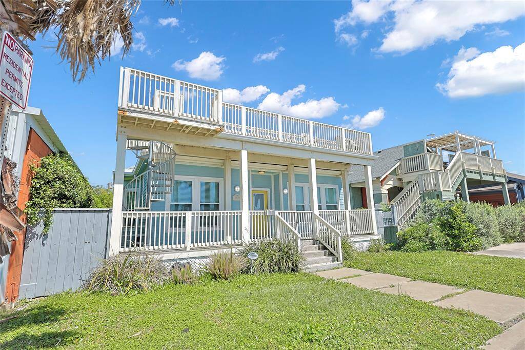 GULF VIEWS FROM THE ROOF TOP DECK!! Charming two-story home with expansive wrap-around balconies, offering ample outdoor space. Features a light blue exterior with white trim and a spiral staircase. Located near Pleasure Pier with a lush green lawn. Ideal for enjoying sunny days.