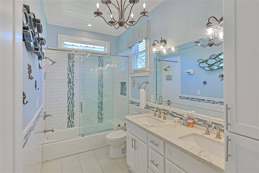 This bathroom features a modern design with a double vanity, elegant fixtures, and a large mirror. The shower-tub combo features a sliding glass door and stylish tile accents.