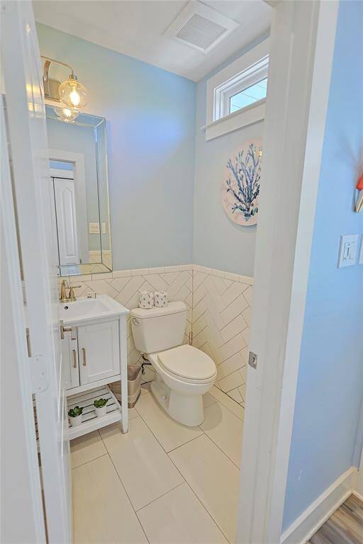 This half bathroom features a designated vanity space and white tile accents. Thoughtfully designated at the back of the home for privacy and convenience.