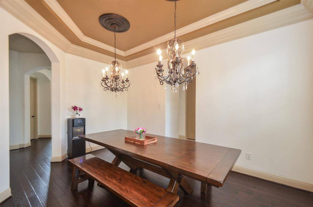 The beauty and versatility of the open floor plan design concept offers timeless utility. Here, the formal dining space, off the main entry walkway, with subtle elegance, pale walls, earth toned tray ceiling, dark flooring and entry/exit space, great when entertaining.