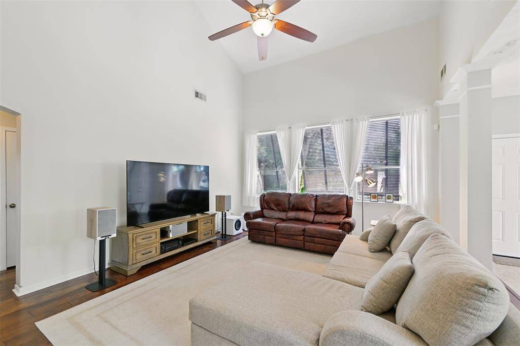 The family room boasts high ceilings, a ceiling fan with an integrated light fixture, and a stunning wall of windows offering a picturesque view of the backyard.
