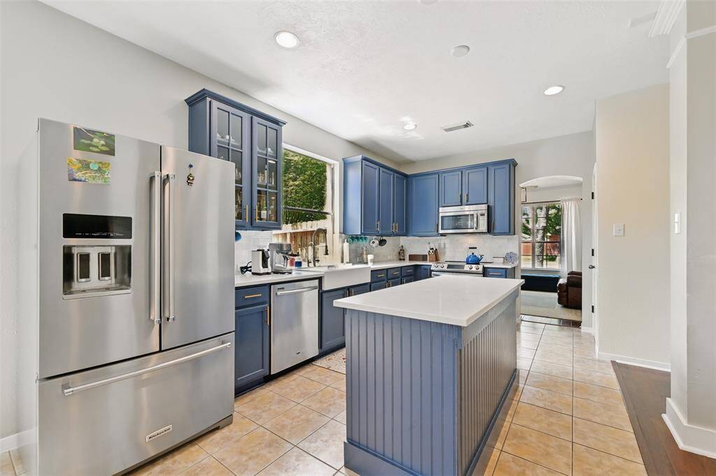 A modern island kitchen featuring stainless steel appliances and tall cabinets with crown molding, including one with elegant glass panels.