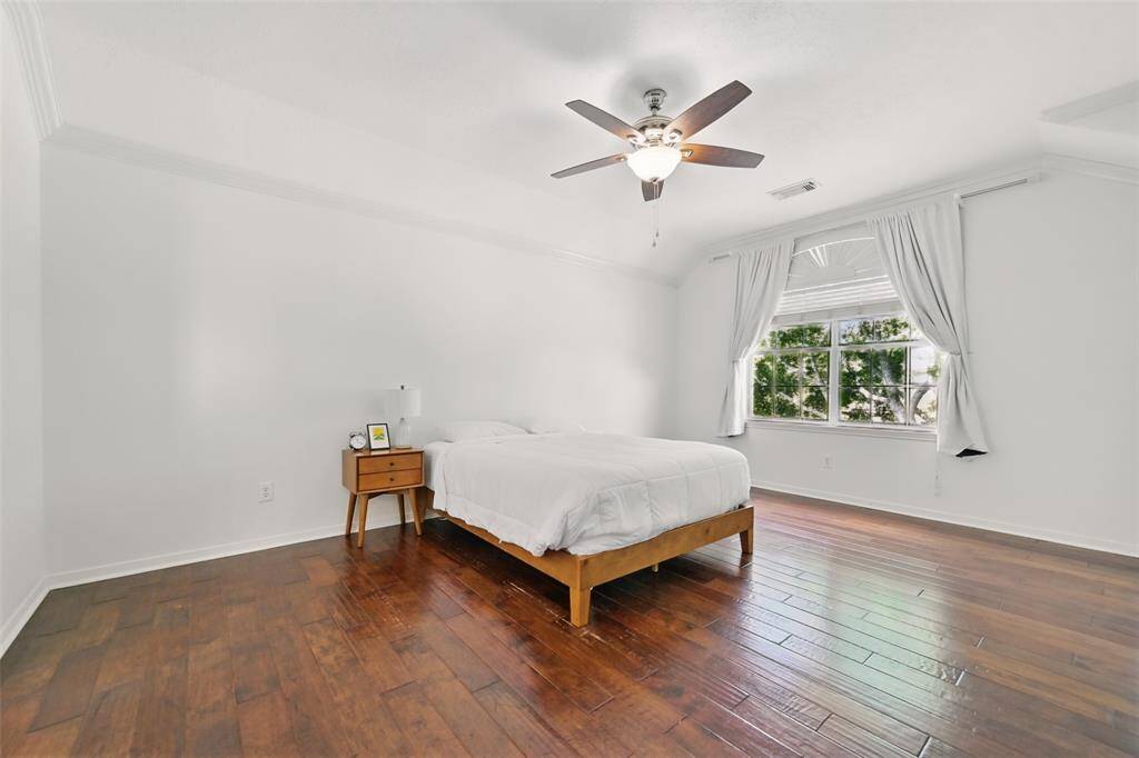 Spacious primary bedroom featuring elegant crown molding, rich wood flooring, and a ceiling fan with an integrated light fixture.