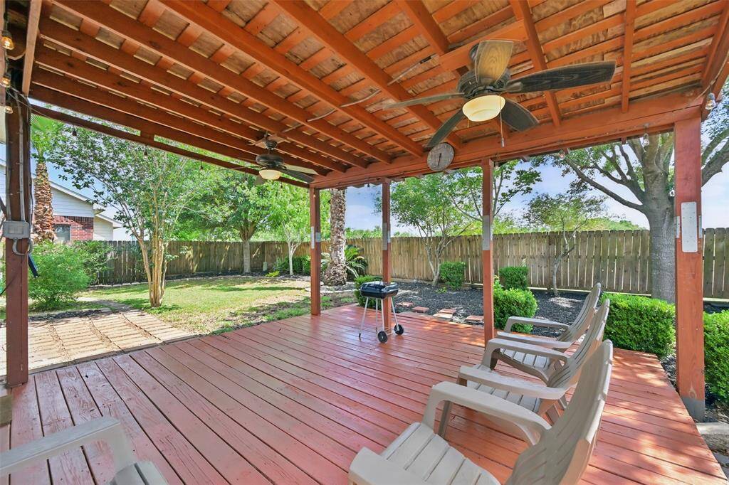 Spacious covered back patio featuring a ceiling fan with an integrated light fixture. The wood deck has been freshly painted, adding a polished touch..