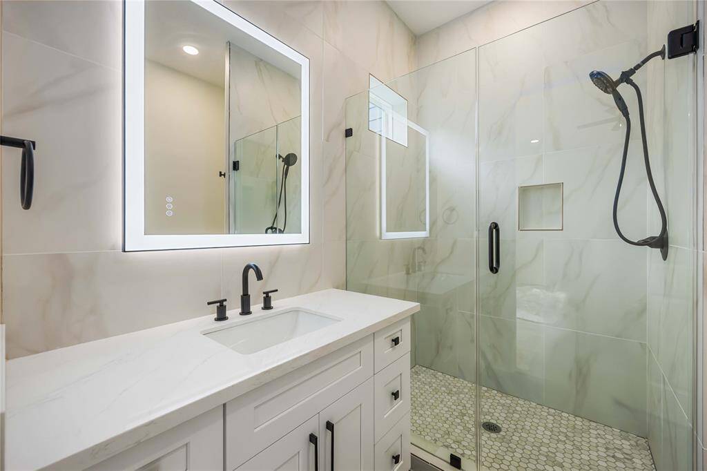 The en-suite bath on the first floor features a large frameless shower, quartz-topped vanity, and an elegant lighted mirror.