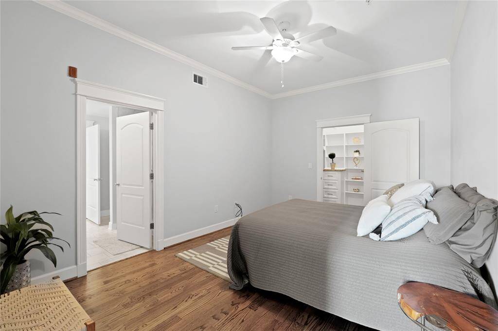 Bedroom featuring hardwood floors, a ceiling fan, oversized closet with built-in shelving, and an en-suite bathroom.