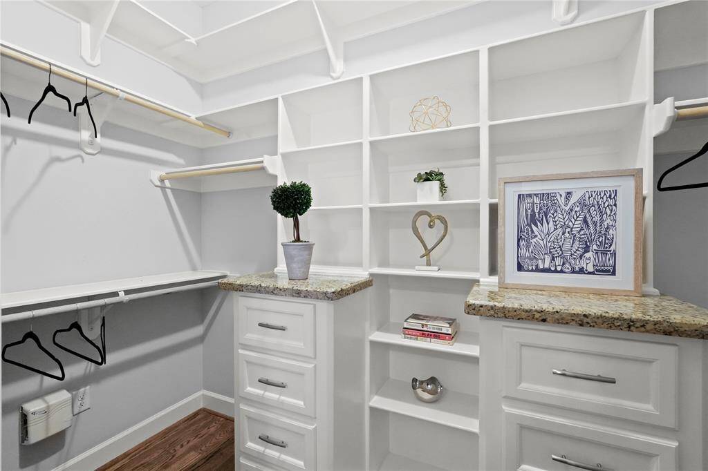 Spacious, well-organized walk-in closet featuring abundant shelving, drawer space, and hanging rods, complemented by a built-in dresser with a granite countertop. The neutral color palette gives it a modern and clean look.