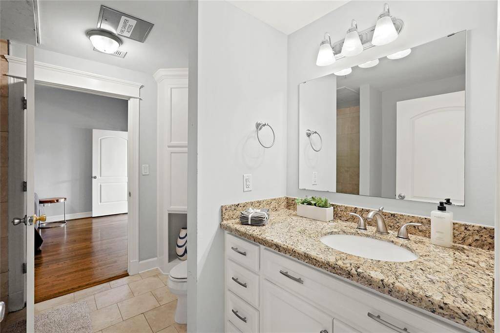 Well-lit bathroom featuring a vanity with granite countertops, ample storage, and a large mirror.