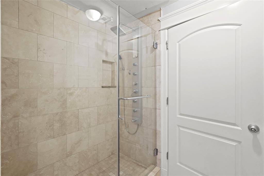 Huge walk-in shower, with frameless  glass door and beige tile walls. There's a built-in niche for toiletries and a multi-jet shower panel.