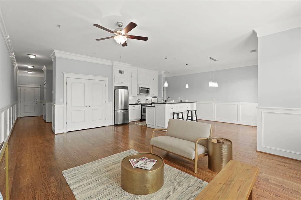 Living area opens to modern kitchen with stainless steel appliances and a breakfast bar. The pantry is stylishly hidden into a wall of cabinets. The room is well-lit and has a neutral color scheme and is finished with elegant wainscoting.