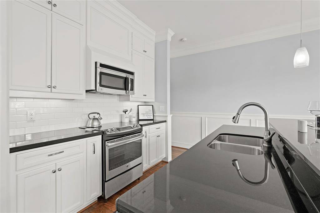 Modern kitchen with white cabinetry, stainless steel appliances, subway tile backsplash, and black countertops, featuring a sleek undermount sink.