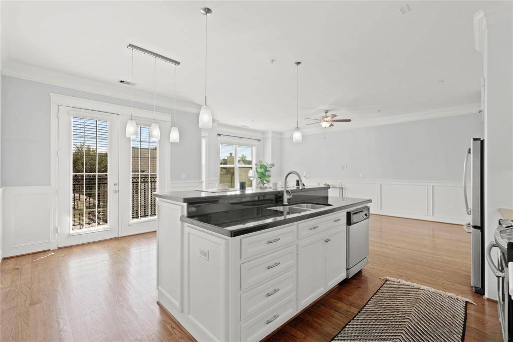 Crisp white cabinetry, central island with a sink, and pendant lighting, opens onto a living space with tall windows and French doors leading to an outdoor area.