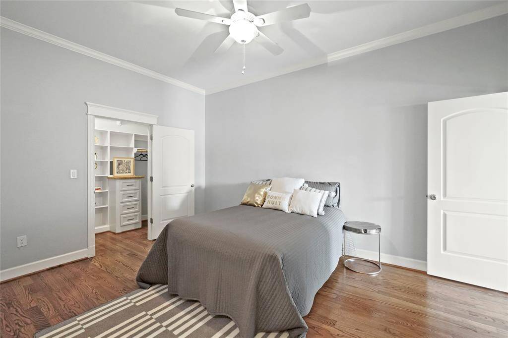 Large bedroom featuring hardwood floors, a ceiling fan, and easy access to a closet with built-ins galore. The room is painted in a soft, neutral color and has a comfortable, contemporary feel.