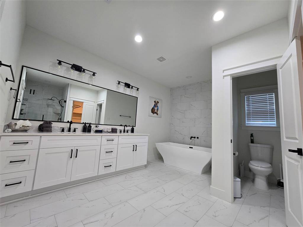 The spacious primary bathroom features dual sinks, a private toilet, and a luxurious standalone soaking tub.