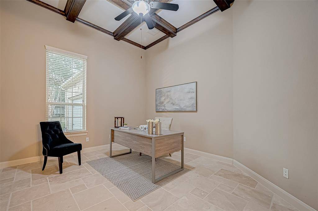 This inviting home office is a blank slate for creativity, featuring a neutral palette, a soothing ceiling fan, and a large window that fills the space with natural light and offers a lovely view of the front yard.