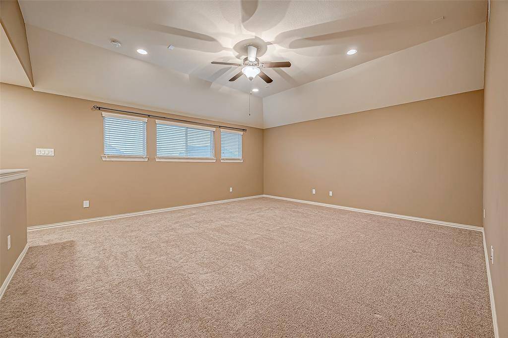 Here's another view of the expansive game room, featuring plush carpeting, a stylish ceiling fan, and windows that invite in plenty of natural light for a bright and cozy atmosphere.