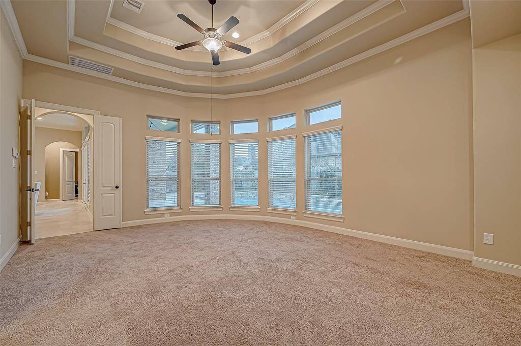The stunning primary bedroom is a luxurious retreat, featuring a curved wall of windows with a gorgeous pool view, an elegant coffered ceiling, and stately French doors for a touch of sophistication.