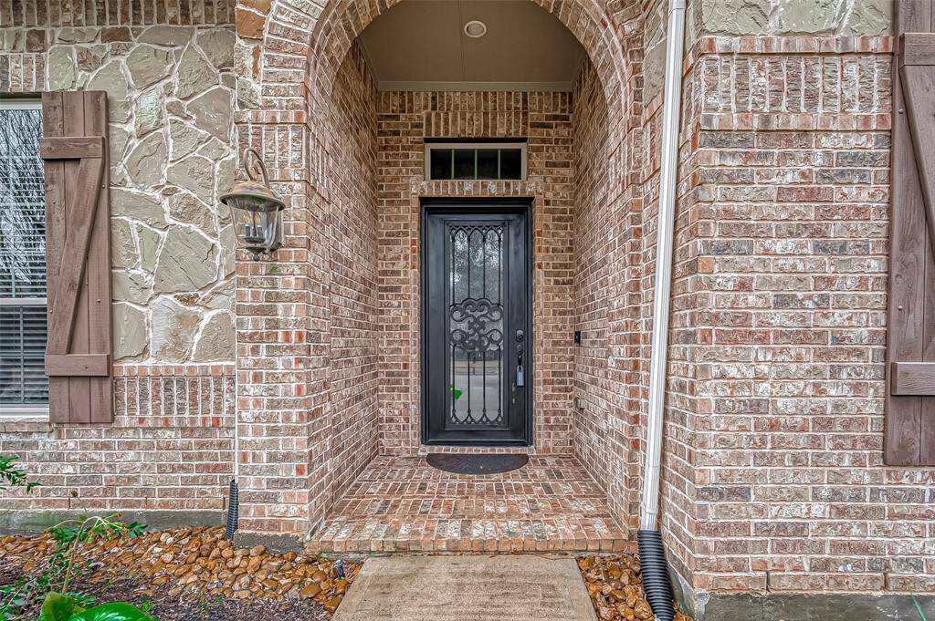 The inviting covered porch, highlighted by a charming carriage-style light and beautiful brickwork, warmly beckons you inside.