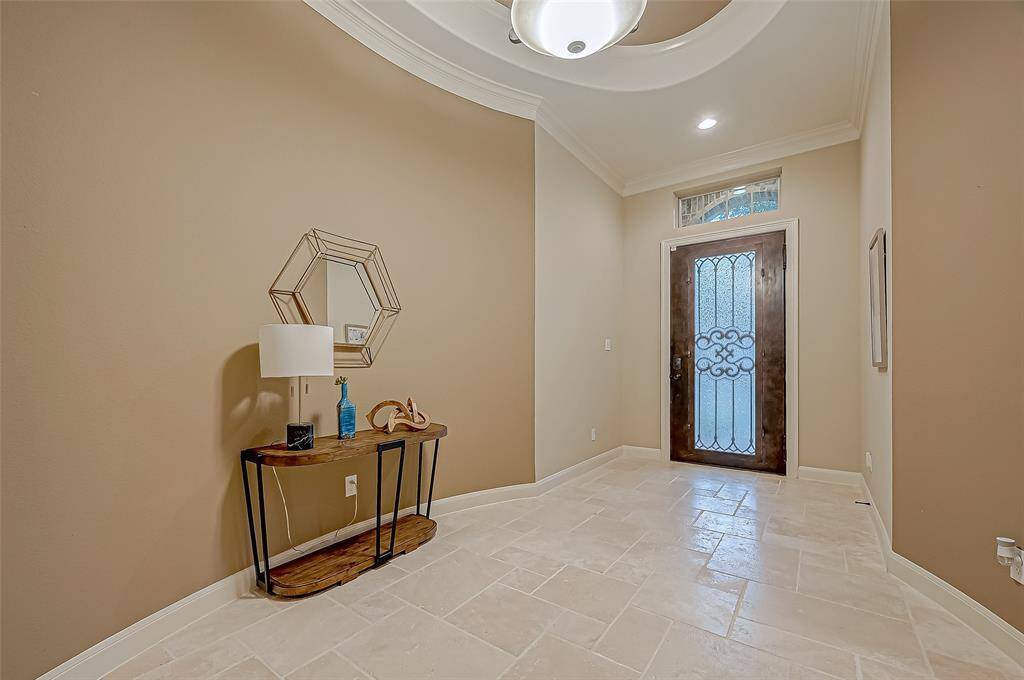 Step into the wide-open foyer, where travertine tile greets you, and an elegant tray ceiling along with a transom window above the beautiful front door create a bright and welcoming first impression.