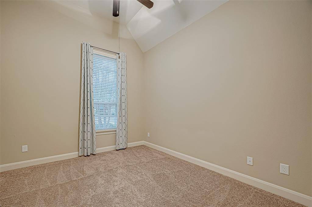 This guest bedroom also offers comfort and charm with a soothing ceiling fan and a large window that fills the space with natural light, creating a warm and inviting retreat.