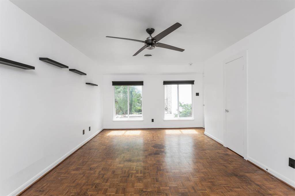 Oversized secondary bedroom on second floor with large windows, drapes, modernized ceiling fan, and floating shelving.