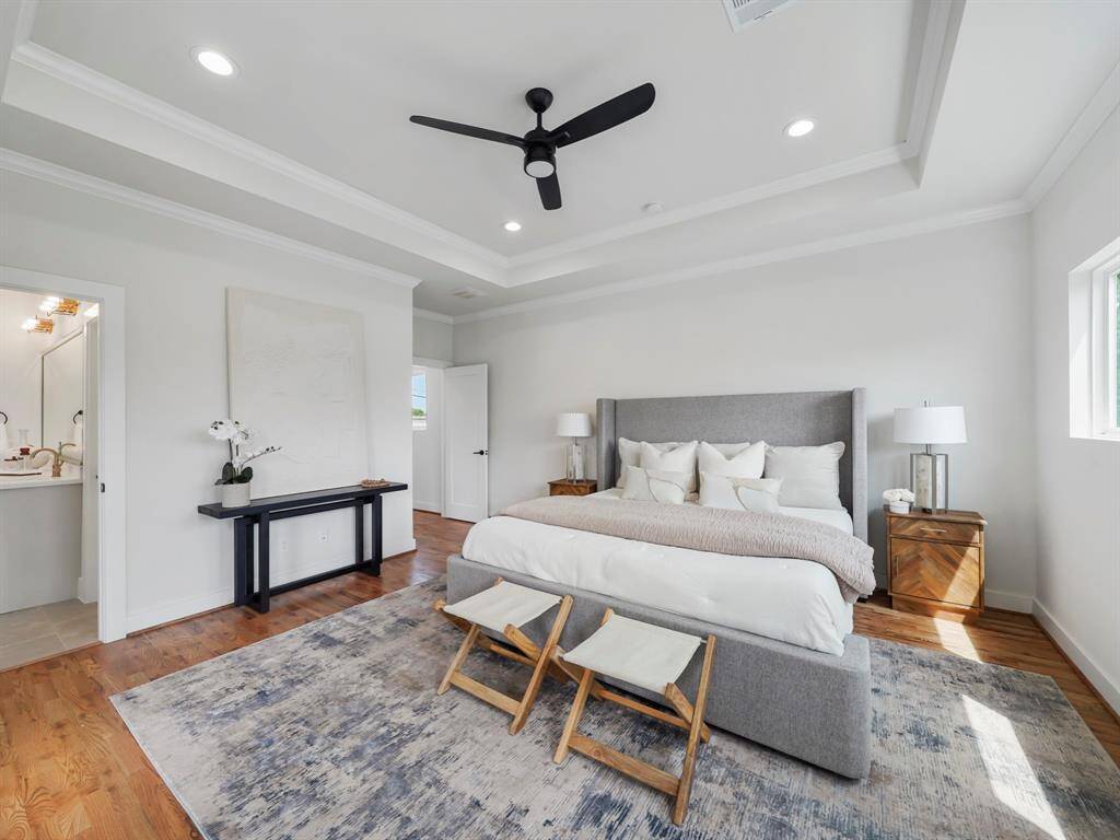 Spacious primary bedroom with a serene atmosphere, featuring a tray ceiling that adds depth and elegance to the room. The ceiling fan enhances comfort while maintaining a modern, stylish touch. Large windows fill the space with natural light, creating a peaceful retreat to unwind and relax.