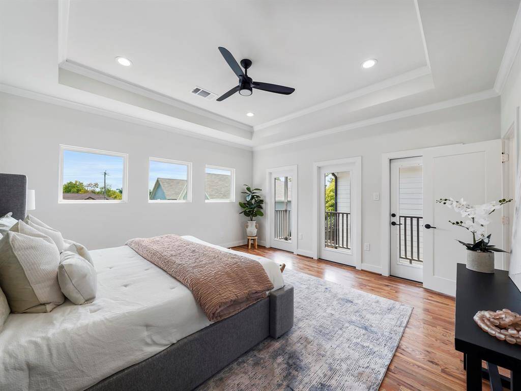 Spacious primary bedroom with a serene atmosphere, featuring a tray ceiling that adds depth and elegance to the room. The ceiling fan enhances comfort while maintaining a modern, stylish touch. Large windows fill the space with natural light, and a private balcony offers a peaceful retreat. The ensuite bathroom completes this luxurious suite, providing a spa-like experience just steps away.