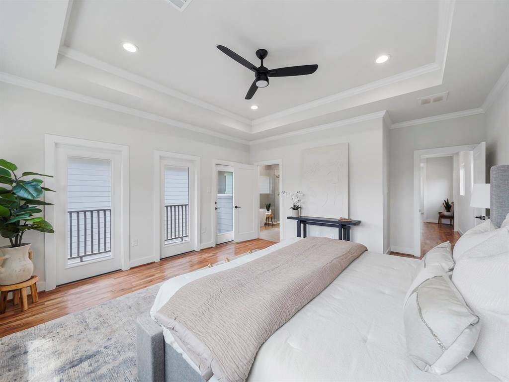 Spacious primary bedroom with a serene atmosphere, featuring a tray ceiling that adds depth and elegance to the room. The ceiling fan enhances comfort while maintaining a modern, stylish touch. Large windows fill the space with natural light, and a private balcony offers a peaceful retreat. The ensuite bathroom completes this luxurious suite, providing a spa-like experience just steps away.