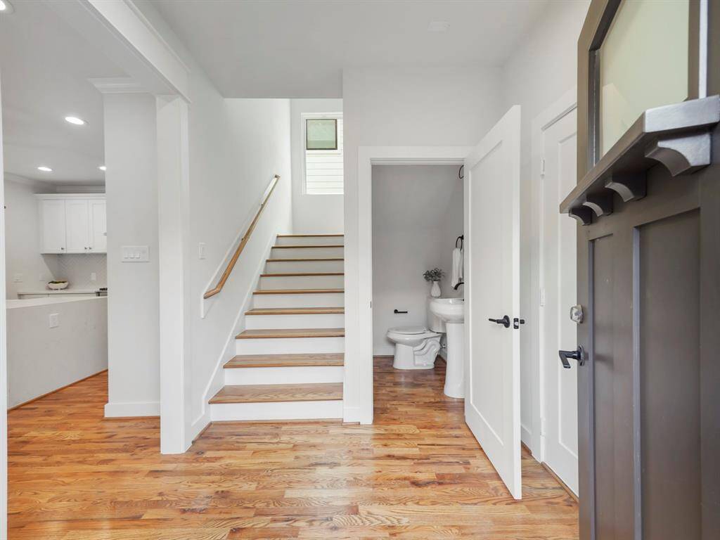 Bright and inviting entryway featuring rich hardwood floors and a functional layout. A stylish half bath offers convenience for guests. The staircase with modern railing leads upstairs, adding to the home’s open and airy feel. To the right, a door provides easy access to the garage, enhancing everyday functionality."