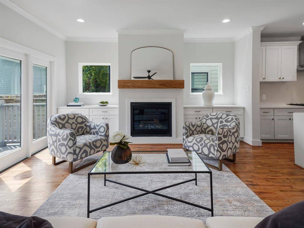 Warm and inviting living room featuring a stunning fireplace as the focal point, framed by custom built-in cabinetry on either side for stylish storage and display. Large windows fill the space with natural light, highlighting the rich hardwood floors and open layout. A perfect blend of comfort and sophistication.