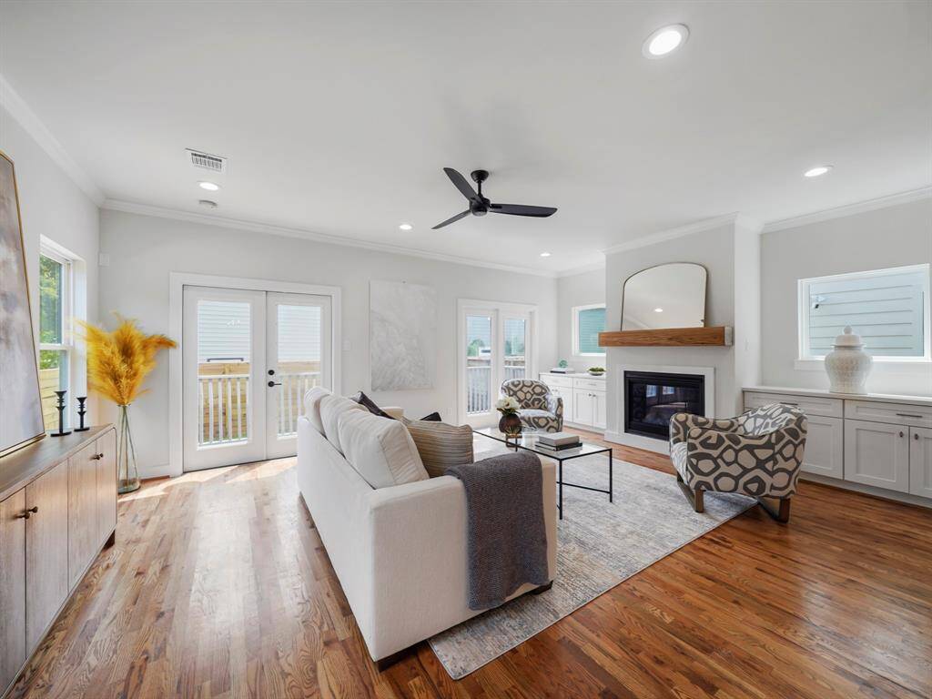 Spacious and light-filled living room showcasing expansive windows that offer stunning views of the backyard. A glass door seamlessly connects indoor and outdoor living, leading to the covered back porch. The open layout, rich hardwood floors, and abundance of natural light create an inviting and airy atmosphere.