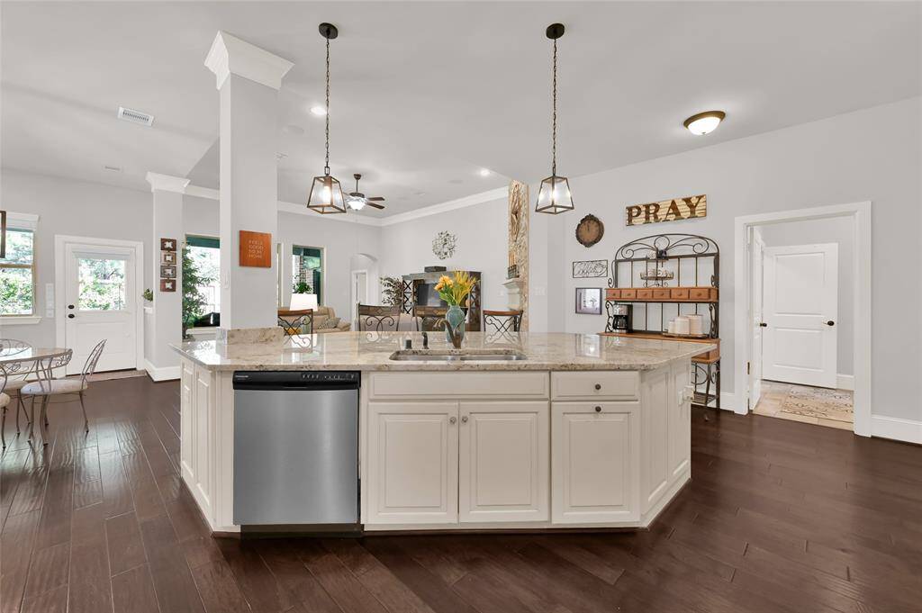 This spacious kitchen features a large island with granite countertops, pendant lighting, and ample white cabinetry. The open layout flows into a bright living area that is perfect for entertaining.