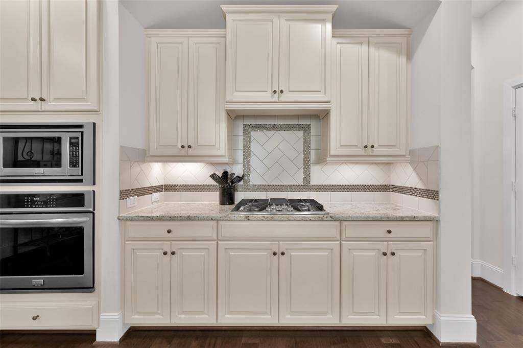 Sleek kitchen with modern appliances, elegant cream cabinetry, and a stylish backsplash. The granite countertop and built-in cooktop add a touch of luxury. Perfect for culinary enthusiasts.