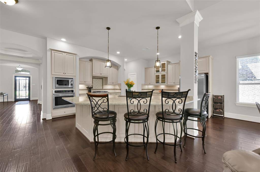 This spacious kitchen features elegant cabinetry, a large island with seating for four, and modern appliances. The open layout and dark hardwood floors create a warm, inviting atmosphere, perfect for entertaining.