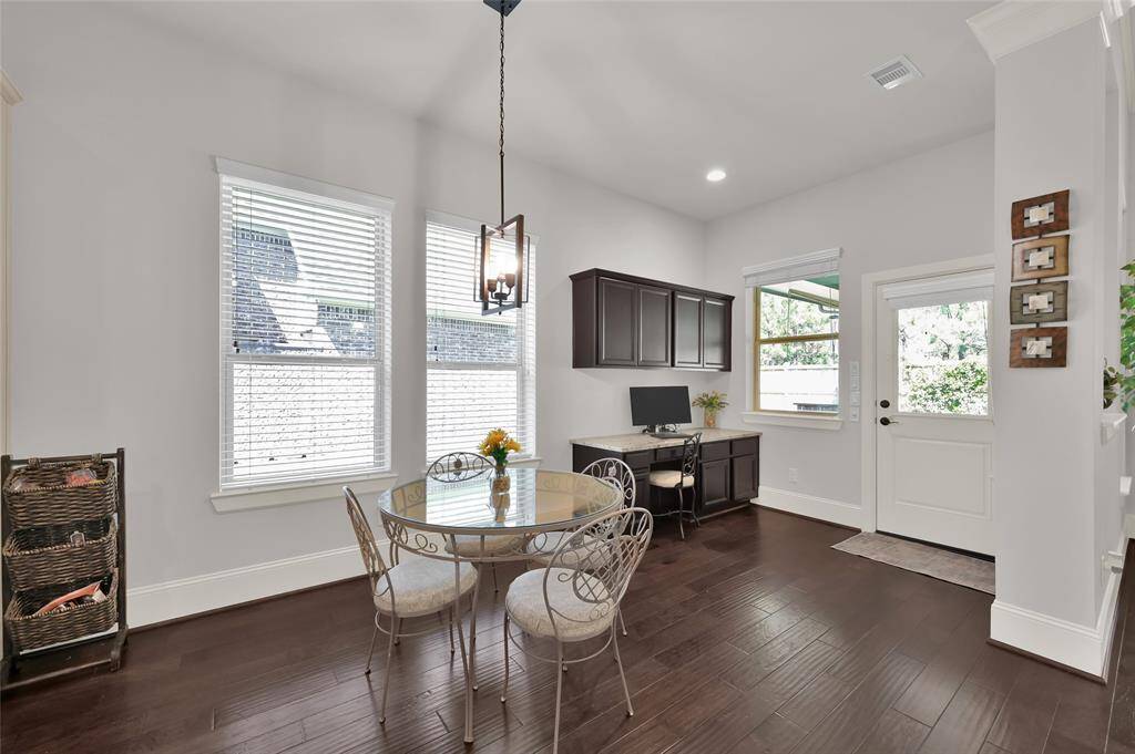 Bright breakfast dining area with dark wood flooring. There's a built-in desk with upper cabinets, a door leading outside, and large windows for natural light.