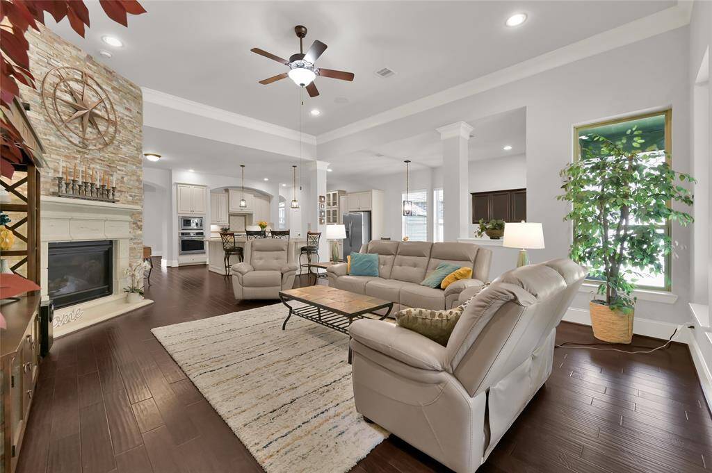 This open-concept living area features a cozy stone fireplace, elegant wood flooring, and ample natural light. The space seamlessly connects to a modern kitchen with a large island, perfect for entertainment and family gatherings.
