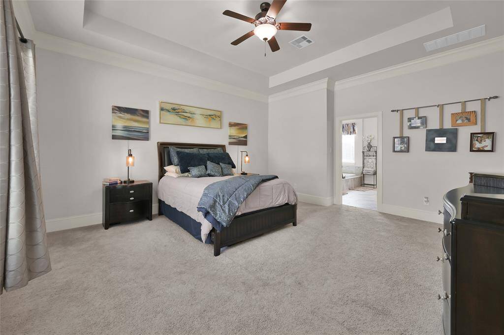 This spacious primary bedroom features carpet, a ceiling fan, and neutral walls. Plenty of room for a king size bed with side tables. The room connects to a bright en-suite bathroom, enhancing convenience and privacy.