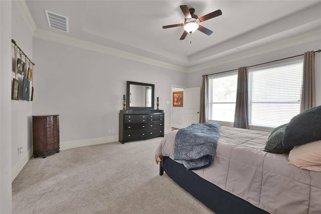 Spacious bedroom with neutral tones, featuring a ceiling fan and large windows for natural light creating a cozy yet elegant atmosphere.