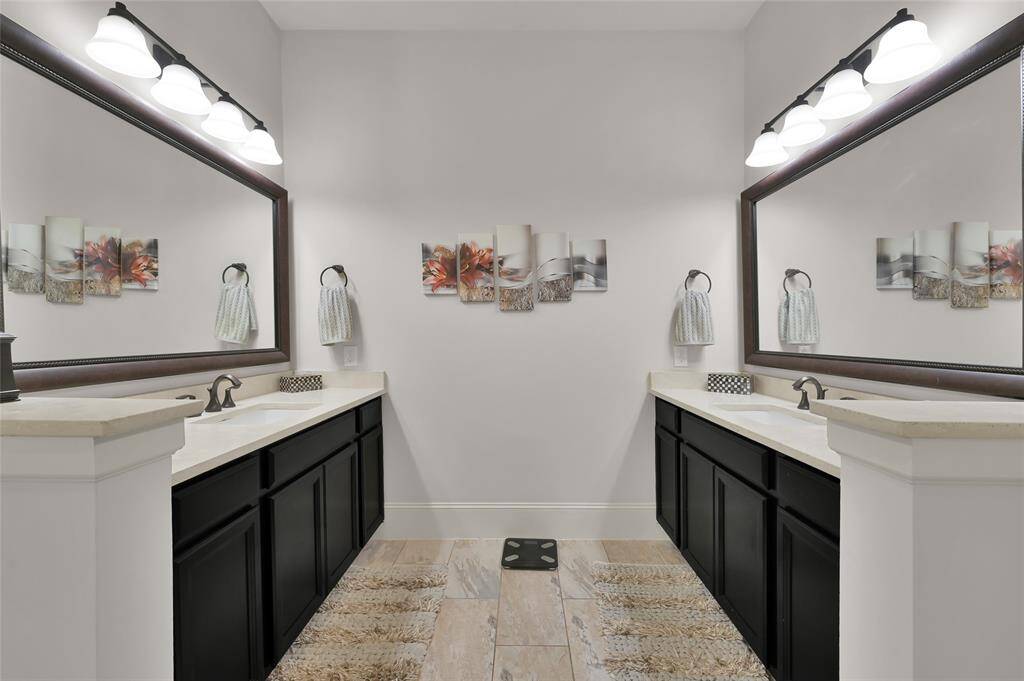 This spacious primary bathroom features dual sinks with dark cabinetry and large mirrors. It has bright lighting, a clean modern aesthetic, providing a comfortable and stylish space.