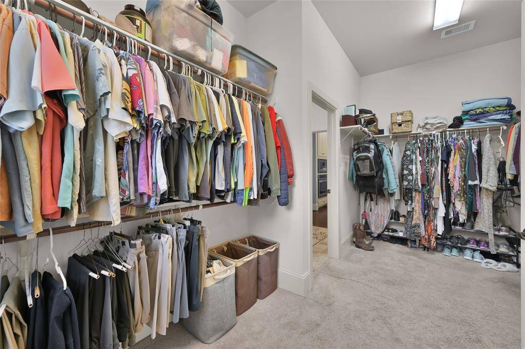 This spacious walk-in closet features ample storage with two levels of hanging rods, shelves for folded items, and additional space for shoes and accessories. It's well-organized and connected to a bathroom, providing convenient access.